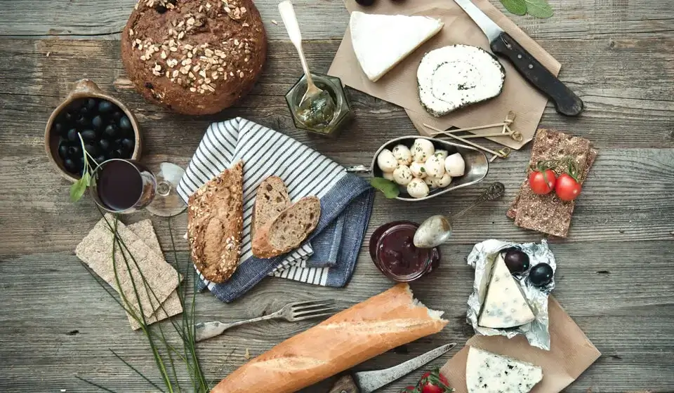 Ein Holztisch mit Roggenbrot, verschiedenen Käsesorten, Wein und Tomaten Ein Holztisch mit Roggenbrot, verschiedenen Käsesorten, Wein und Tomaten